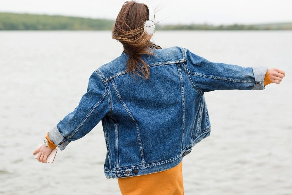 Woman wearing a classic blue denim jacket by the lakeside, casual 2026 fashion style